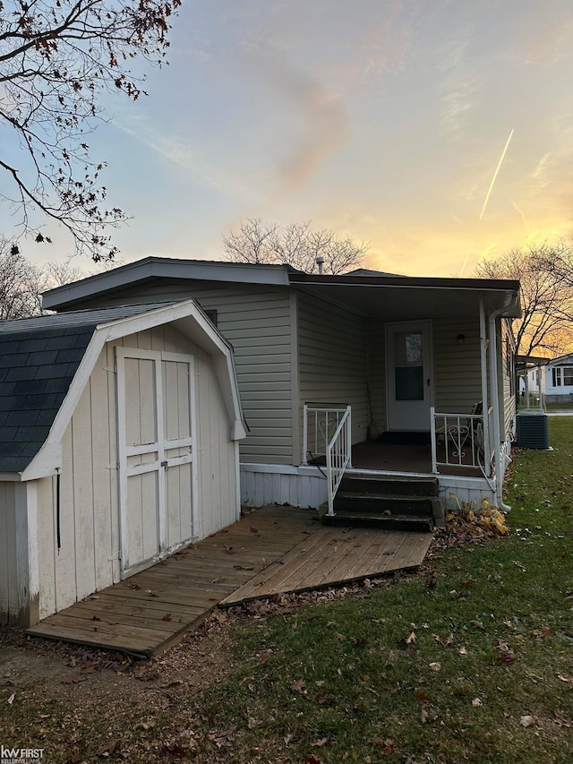 back house at dusk with a porch, a shed, and central AC