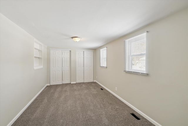 unfurnished bedroom with visible vents, baseboards, multiple closets, and carpet flooring