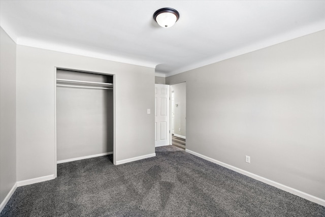 unfurnished bedroom featuring dark colored carpet, a closet, and baseboards