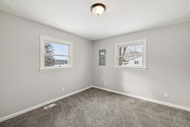 empty room with electric panel, visible vents, dark colored carpet, and a wealth of natural light