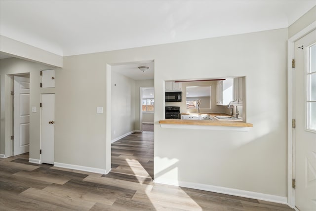 kitchen with black microwave, wood finished floors, a sink, and range