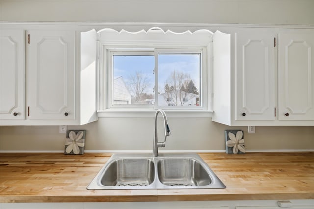 kitchen with white cabinetry, wooden counters, and a sink