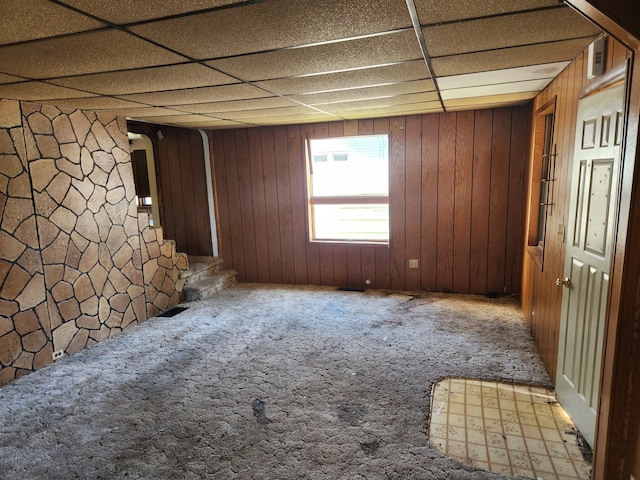 unfurnished room featuring carpet flooring, a drop ceiling, and wooden walls