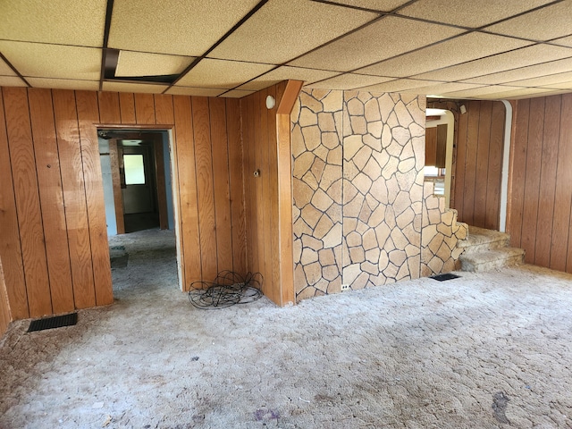 carpeted empty room featuring a paneled ceiling and wood walls