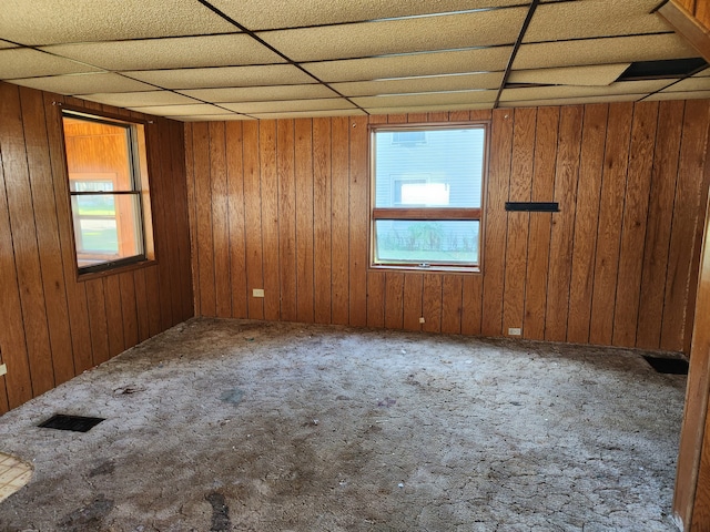 carpeted spare room with wooden walls, plenty of natural light, and a drop ceiling