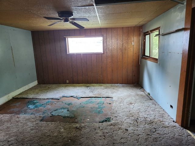 carpeted spare room featuring a paneled ceiling, ceiling fan, and wooden walls