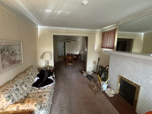 carpeted living room featuring ceiling fan, ornamental molding, and a brick fireplace