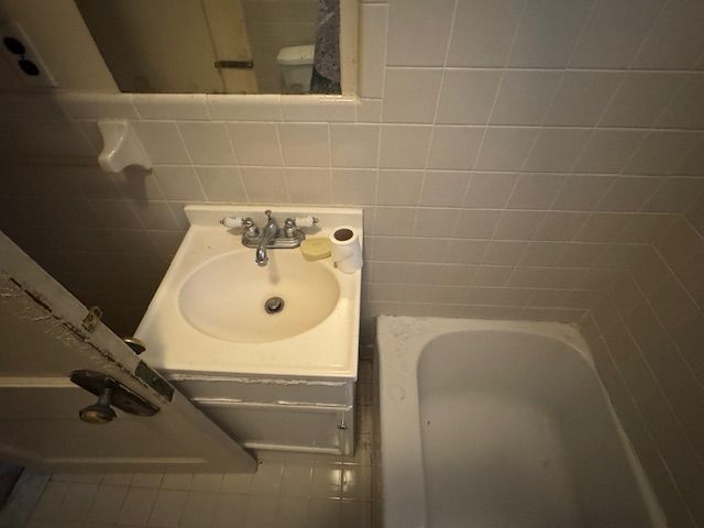 bathroom with a washtub, tile walls, and vanity