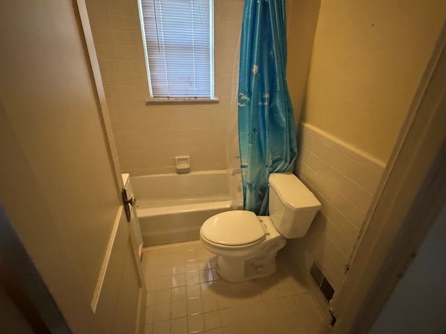 bathroom featuring tile patterned floors, shower / bath combination with curtain, toilet, and tile walls