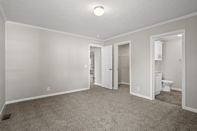 unfurnished bedroom with carpet flooring, ensuite bath, a spacious closet, crown molding, and a textured ceiling