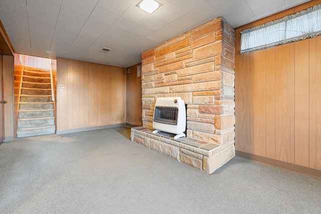 unfurnished living room with heating unit, wooden walls, and light colored carpet