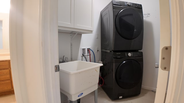 clothes washing area with cabinets, stacked washing maching and dryer, light tile patterned flooring, and sink