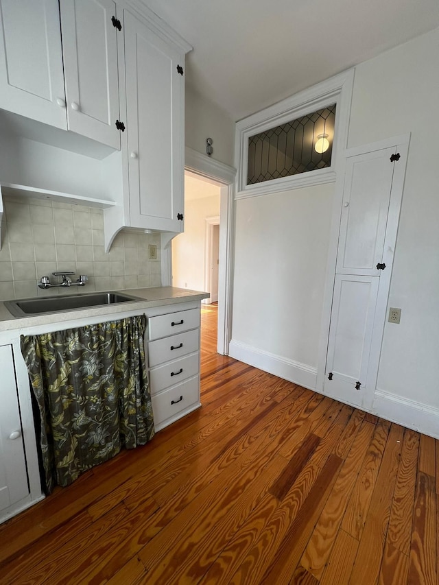 kitchen with backsplash, white cabinetry, sink, and light hardwood / wood-style flooring