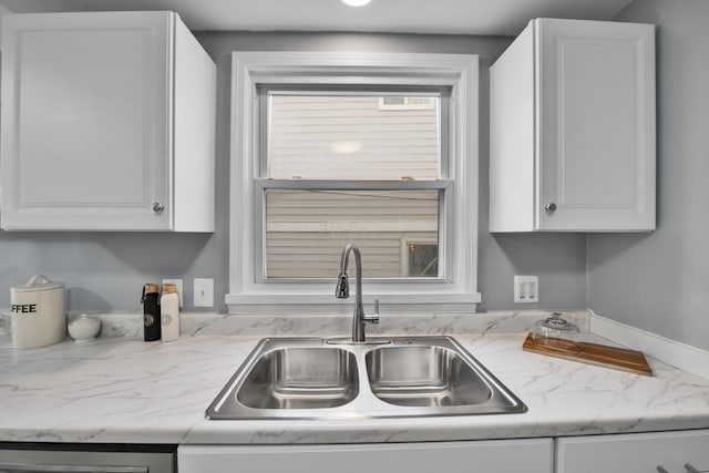 kitchen featuring white cabinets, light stone counters, and sink