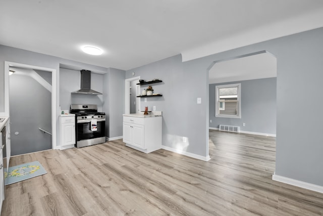 kitchen with stainless steel gas range oven, light hardwood / wood-style flooring, white cabinets, and wall chimney range hood