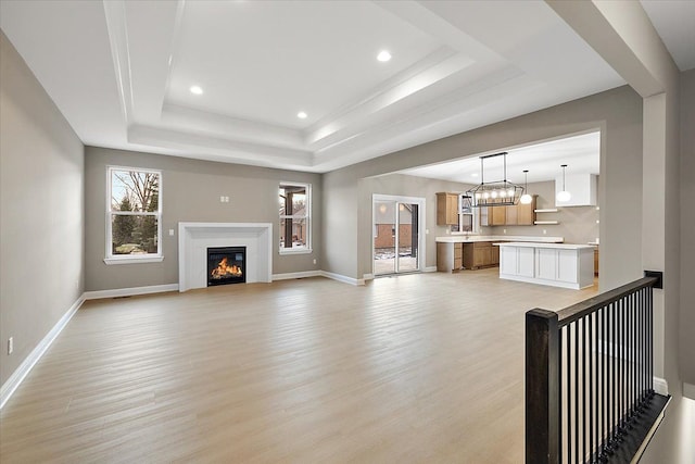 unfurnished living room with an inviting chandelier, a tray ceiling, and light hardwood / wood-style flooring