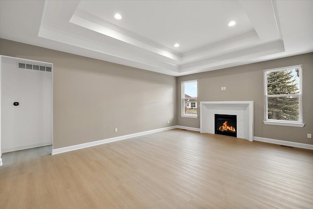 unfurnished living room featuring a tray ceiling, light hardwood / wood-style flooring, and a healthy amount of sunlight