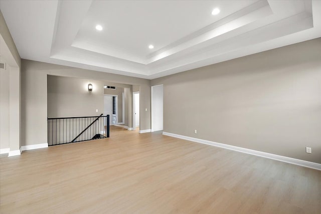 empty room with a tray ceiling and light hardwood / wood-style flooring