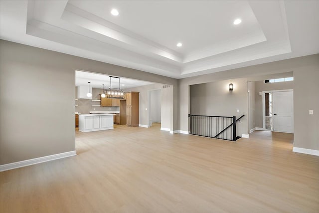 unfurnished living room featuring a raised ceiling and light hardwood / wood-style flooring