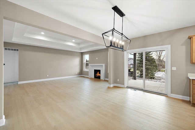 unfurnished living room with an inviting chandelier, light wood-type flooring, and a tray ceiling