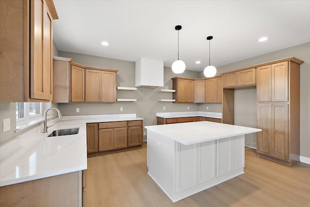 kitchen featuring sink, a kitchen island, decorative light fixtures, and light hardwood / wood-style flooring