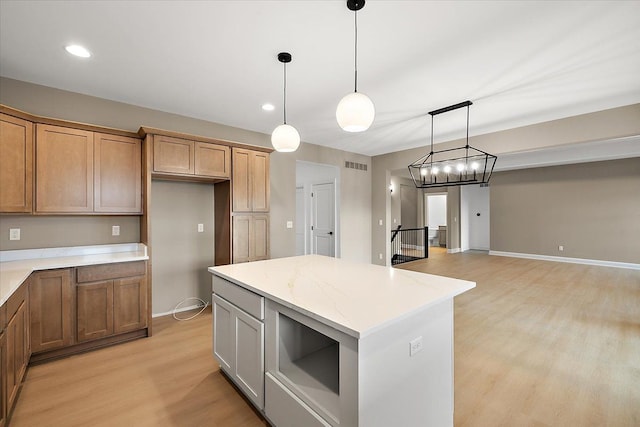 kitchen with decorative light fixtures, a center island, light stone countertops, and light hardwood / wood-style flooring