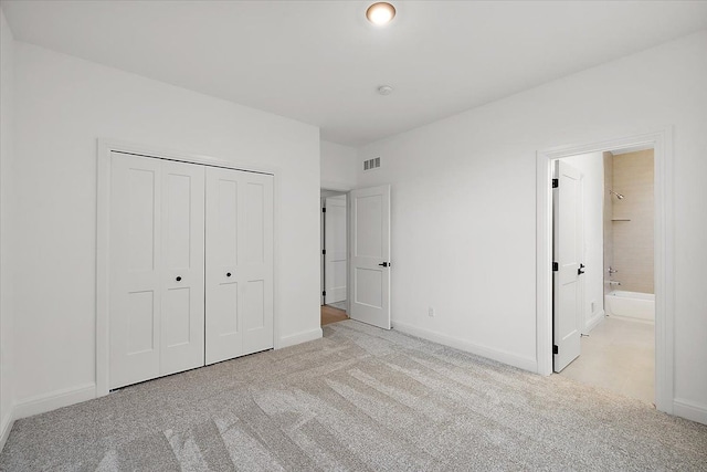 unfurnished bedroom with ensuite bathroom, a closet, and light colored carpet