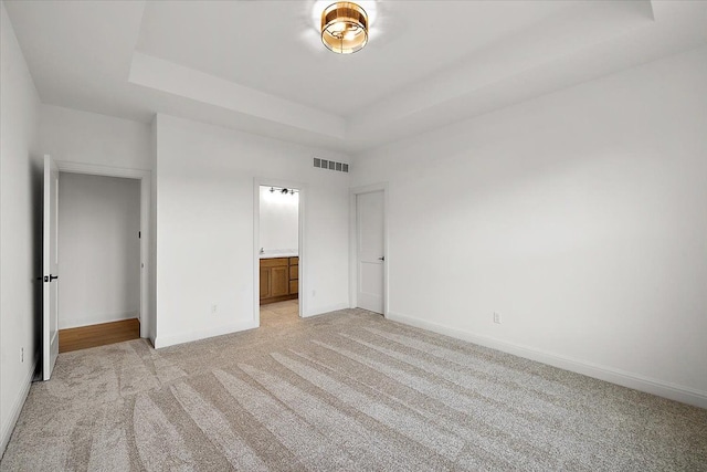 unfurnished bedroom featuring ensuite bathroom, light carpet, and a tray ceiling