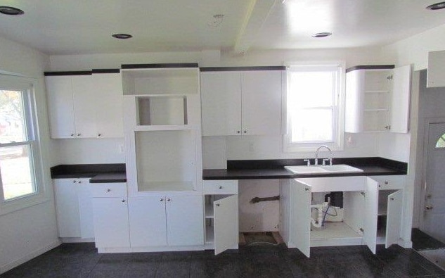 kitchen featuring dark tile patterned flooring, white cabinetry, a healthy amount of sunlight, and sink