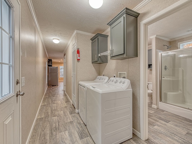 clothes washing area with cabinets, washer and dryer, light wood-type flooring, a textured ceiling, and ornamental molding