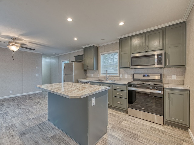 kitchen with appliances with stainless steel finishes, ornamental molding, sink, gray cabinets, and a kitchen island