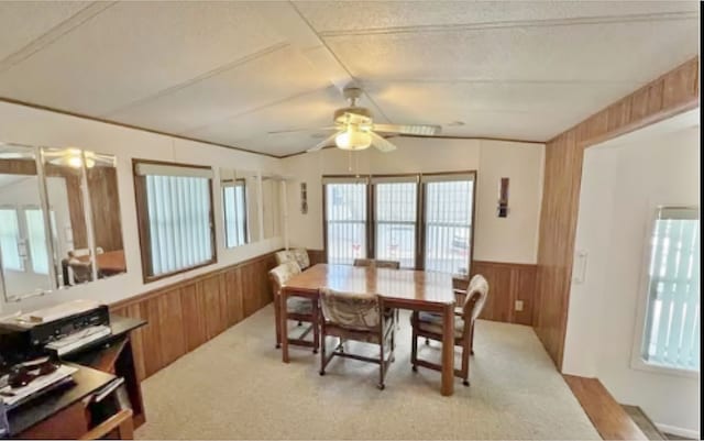 carpeted dining area featuring ceiling fan, a healthy amount of sunlight, a textured ceiling, and wooden walls