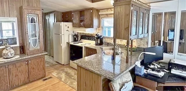 kitchen with sink, light stone counters, light hardwood / wood-style floors, white appliances, and wooden walls