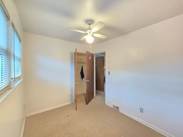 unfurnished bedroom with a closet, light colored carpet, and ceiling fan