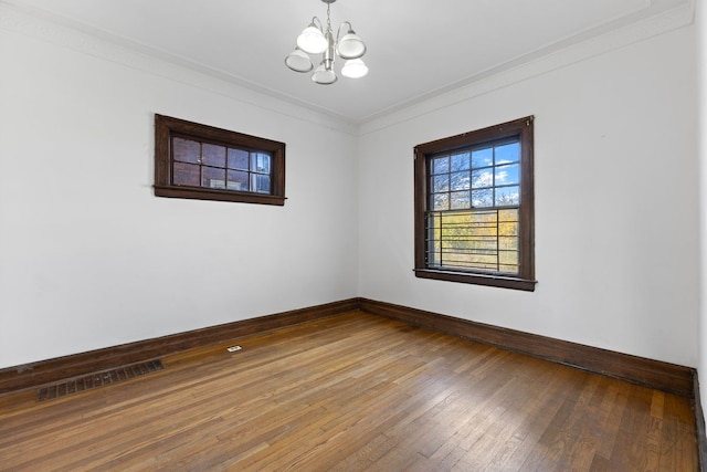 unfurnished room featuring hardwood / wood-style flooring, crown molding, and an inviting chandelier