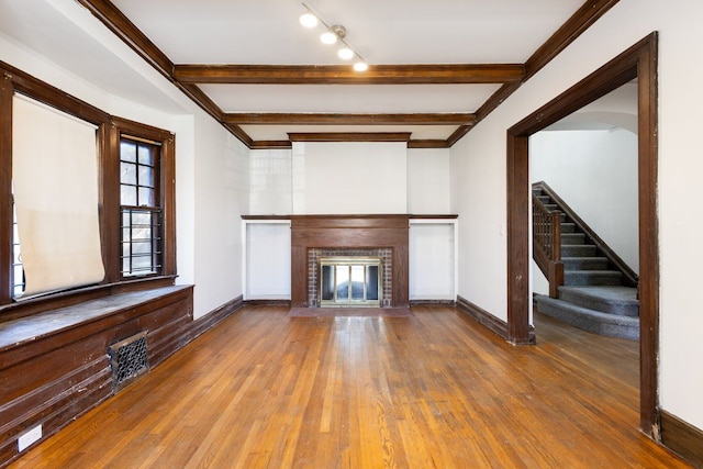 unfurnished living room with rail lighting, a brick fireplace, beamed ceiling, hardwood / wood-style floors, and ornamental molding