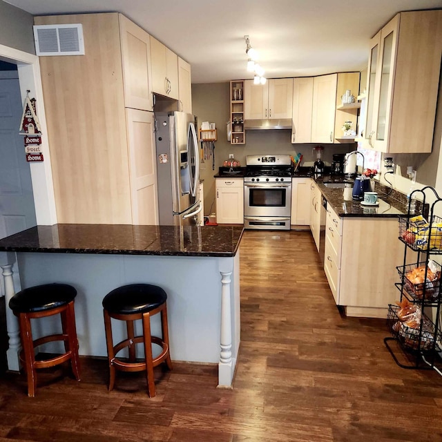 kitchen with sink, stainless steel appliances, dark hardwood / wood-style flooring, kitchen peninsula, and dark stone counters