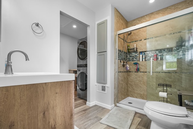 bathroom with sink, hardwood / wood-style flooring, stacked washer and clothes dryer, toilet, and a shower with shower door