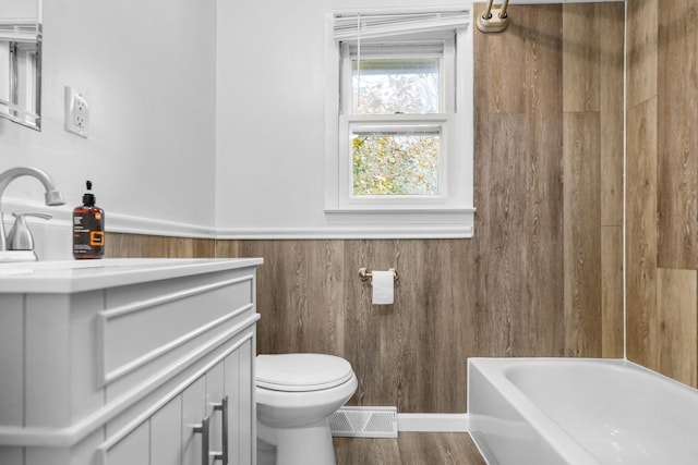 bathroom featuring a washtub, wood-type flooring, toilet, wooden walls, and vanity