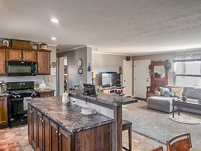 kitchen featuring a kitchen bar, light carpet, dark stone counters, black appliances, and a center island