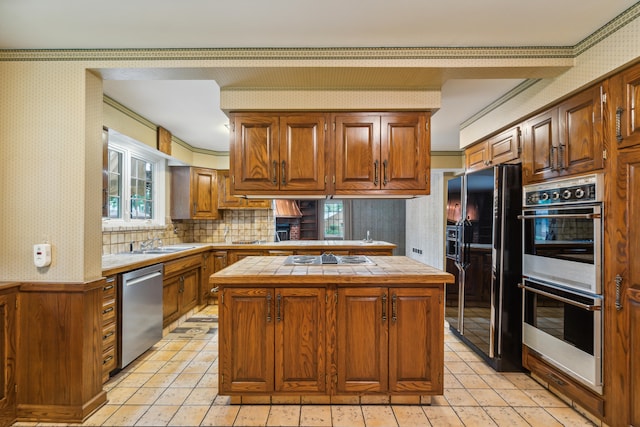 kitchen featuring sink, a center island, tile countertops, appliances with stainless steel finishes, and ornamental molding