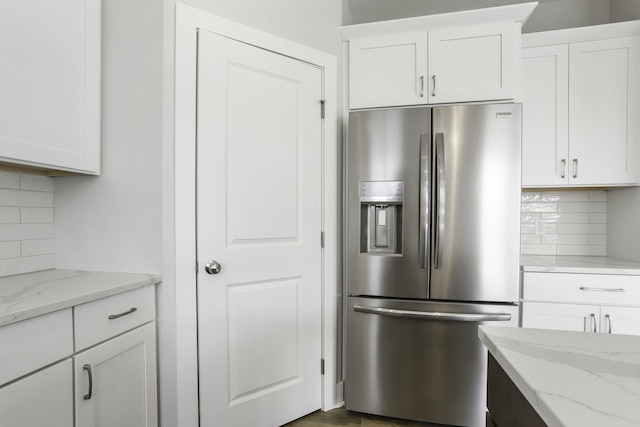 kitchen with light stone countertops, stainless steel refrigerator with ice dispenser, tasteful backsplash, and white cabinetry