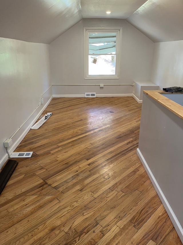 additional living space with wood-type flooring and vaulted ceiling