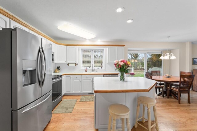 kitchen with appliances with stainless steel finishes, pendant lighting, white cabinetry, sink, and a center island