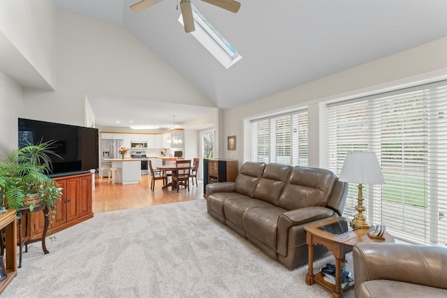 living room featuring light hardwood / wood-style flooring, a skylight, high vaulted ceiling, and ceiling fan