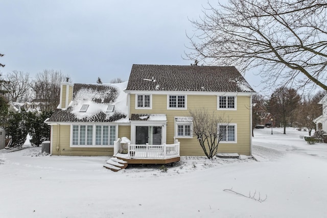 snow covered back of property with central AC and a deck