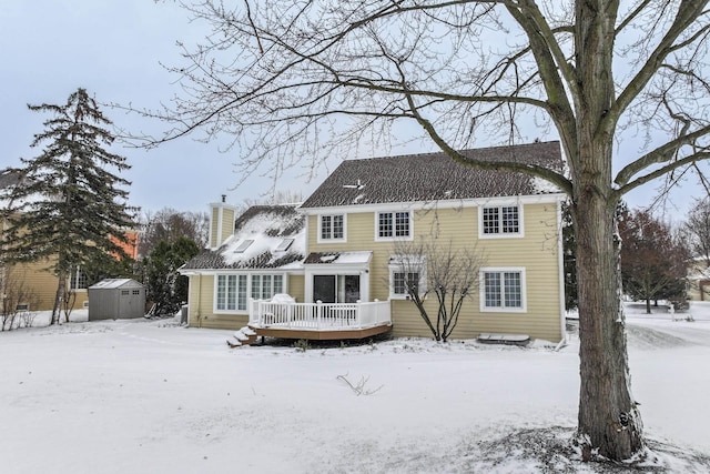 snow covered back of property featuring a storage shed and a deck