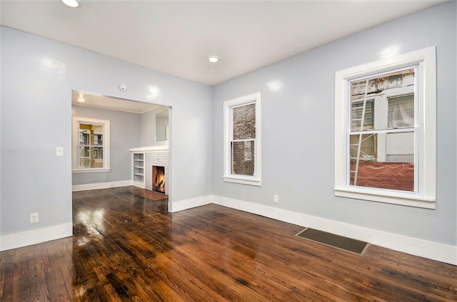 unfurnished living room featuring hardwood / wood-style flooring, a brick fireplace, visible vents, and baseboards