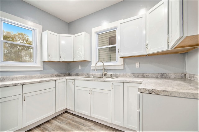 kitchen with white cabinets, light wood-style flooring, light countertops, and a sink