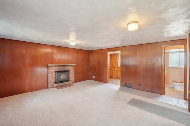 unfurnished living room featuring light colored carpet, a brick fireplace, and wooden walls